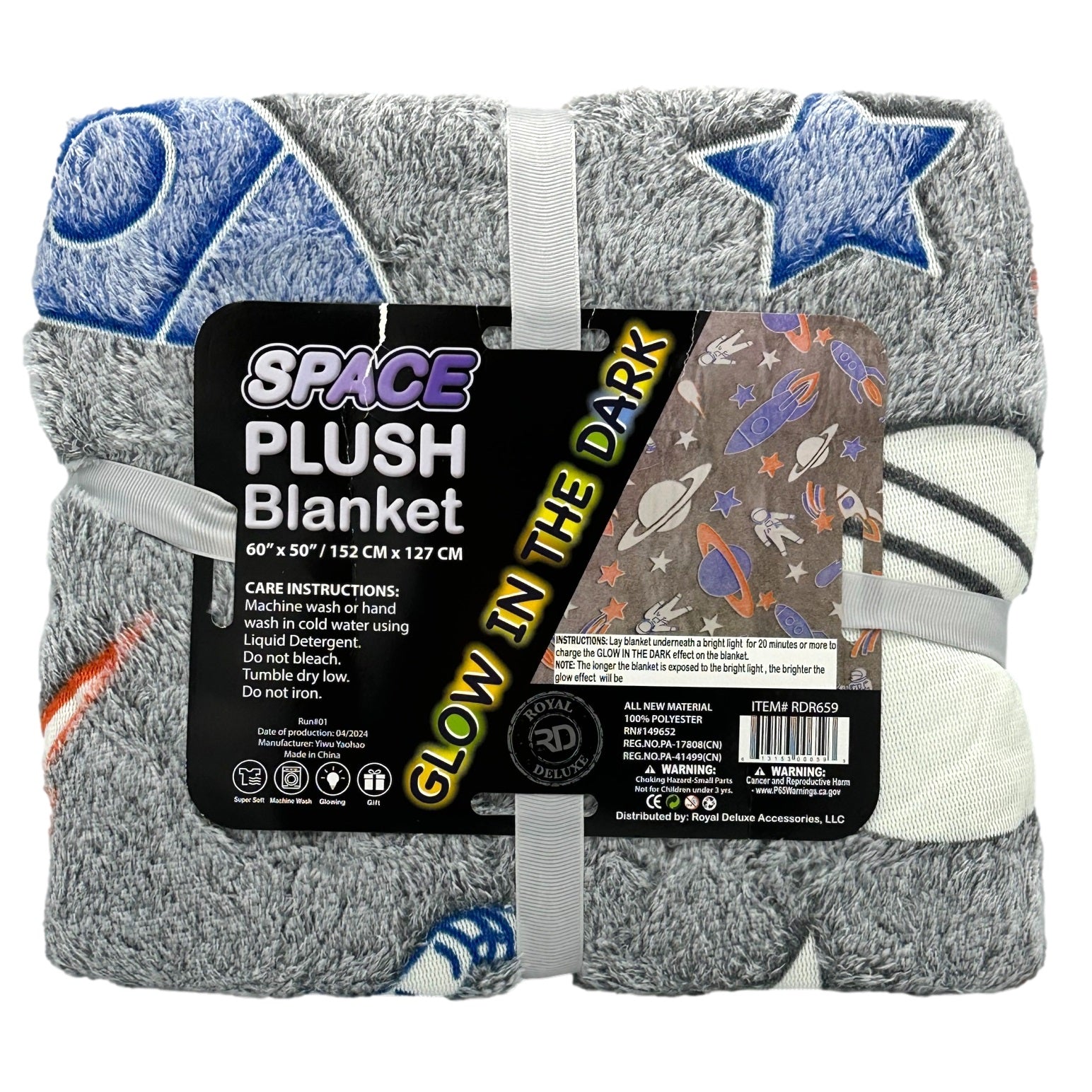 Folded gray plush blanket with space-themed patterns, including stars and rockets, secured with a white ribbon and a label advertising its "Glow in the Dark" feature.